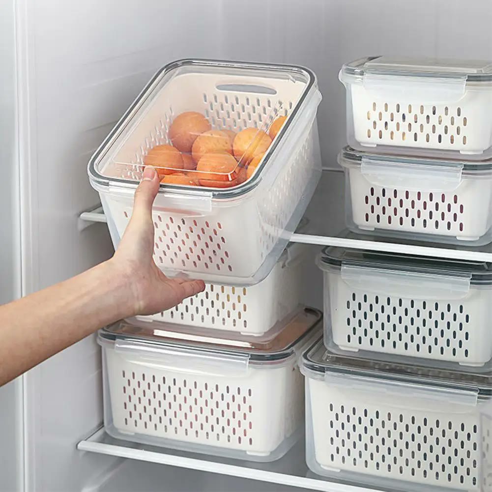 A hand lifting one keeper off a fridge shelf stacked with six others, the white perforated basket visible through the clear outer box